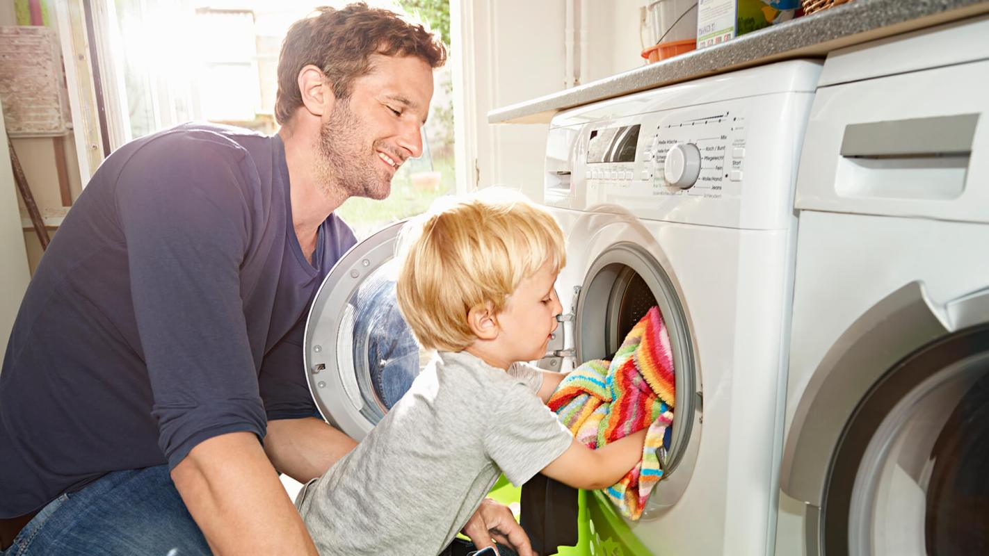 Father and son loading washing machine using green laundry detergents