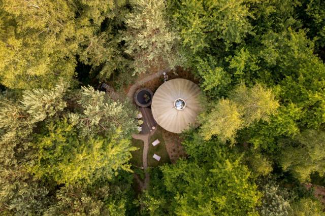 The circular tent structure doesn't seem out of place in its setting, surrounded by lush green forest.