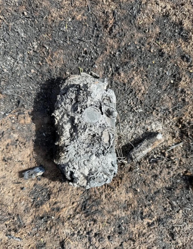A trail camera on the ground covered in ash and debris.