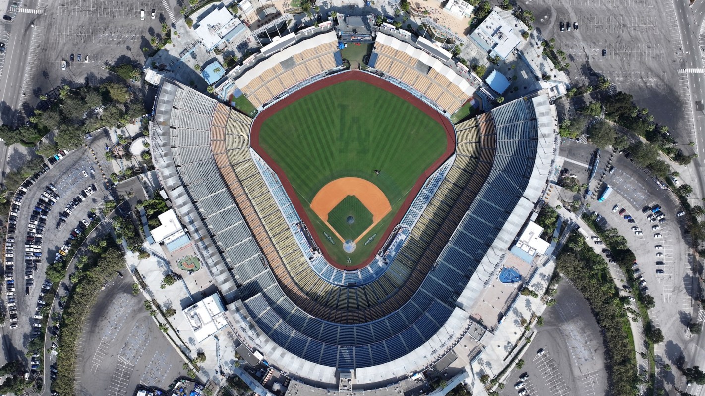 An aerial view of Dodger Stadium, with the Los Angeles Dodgers logo in the outfield grass, and surrounding parking lots.