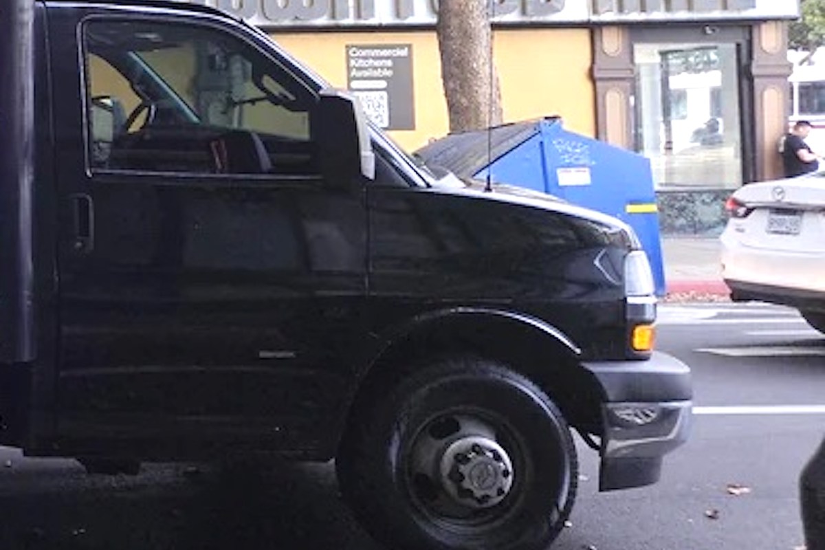 A black truck parked next to a blue dumpster.