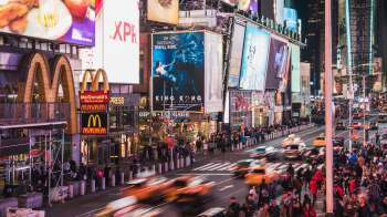 A bustling Times Square at night, featuring bright advertisements and crowds in motion.