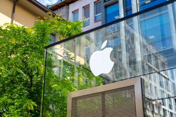 A glass Apple store facade surrounded by lush greenery and buildings reflecting in the glass.