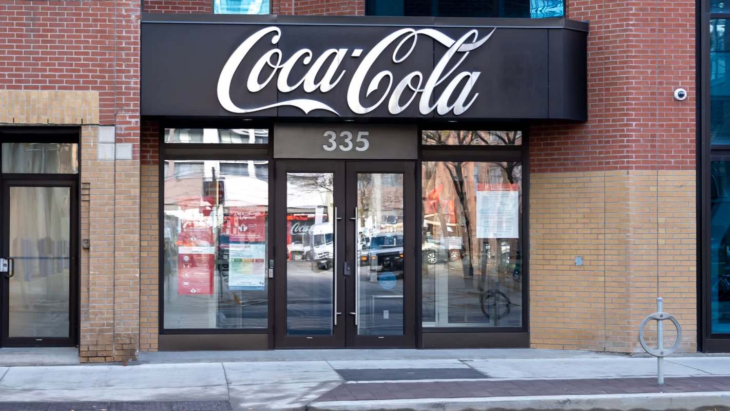 A Coca-Cola storefront featuring large signage and glass doors in a brick building.