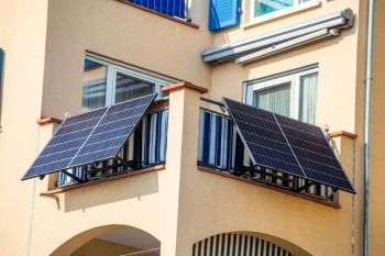 Two solar panels installed on a balcony of a beige apartment building.