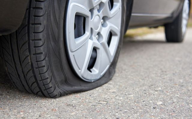 A close-up of a flat tire on a vehicle parked on a gravel road.