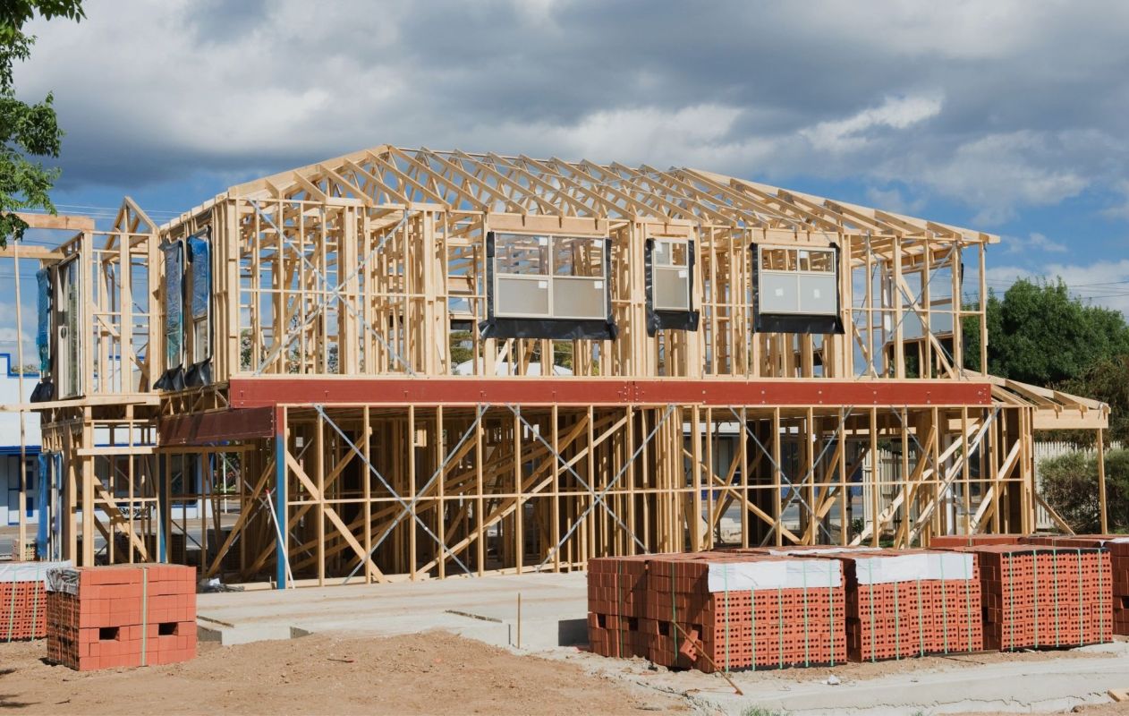 Developers building a partially constructed wooden frame building under a cloudy sky.
