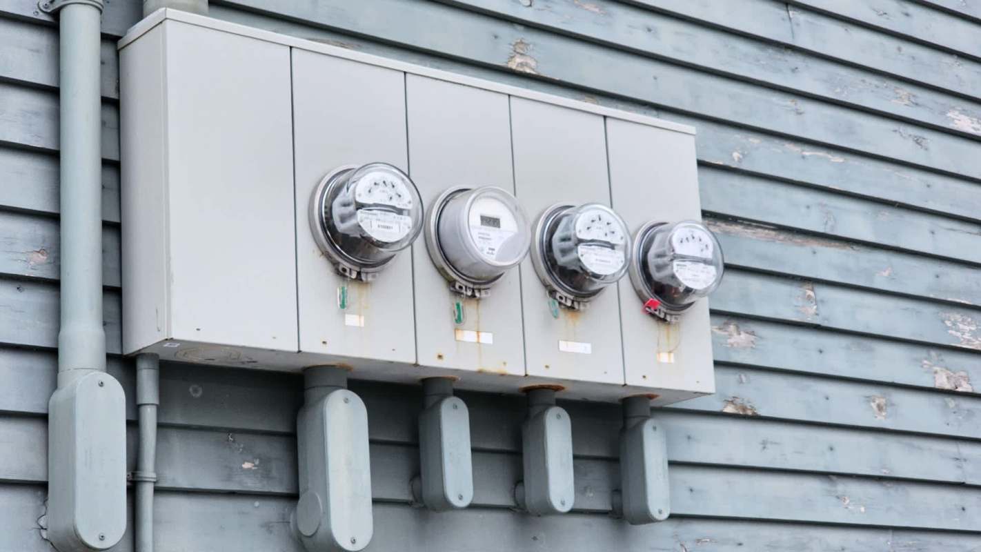 Four electric meters mounted on a gray wall with visible wear and tear.