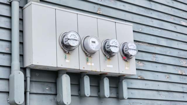 Four electric meters mounted on a gray wall with visible wear and tear.