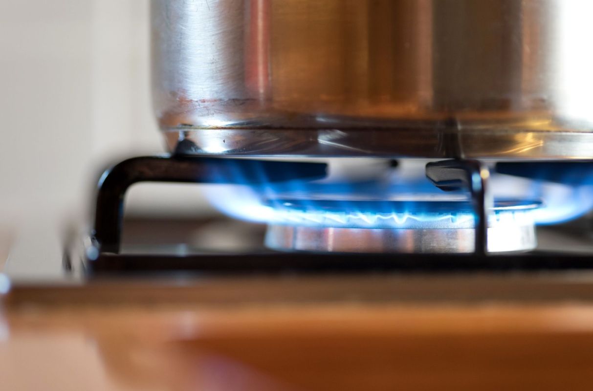 A close-up of a pot on a gas stove with blue flames burning beneath it.