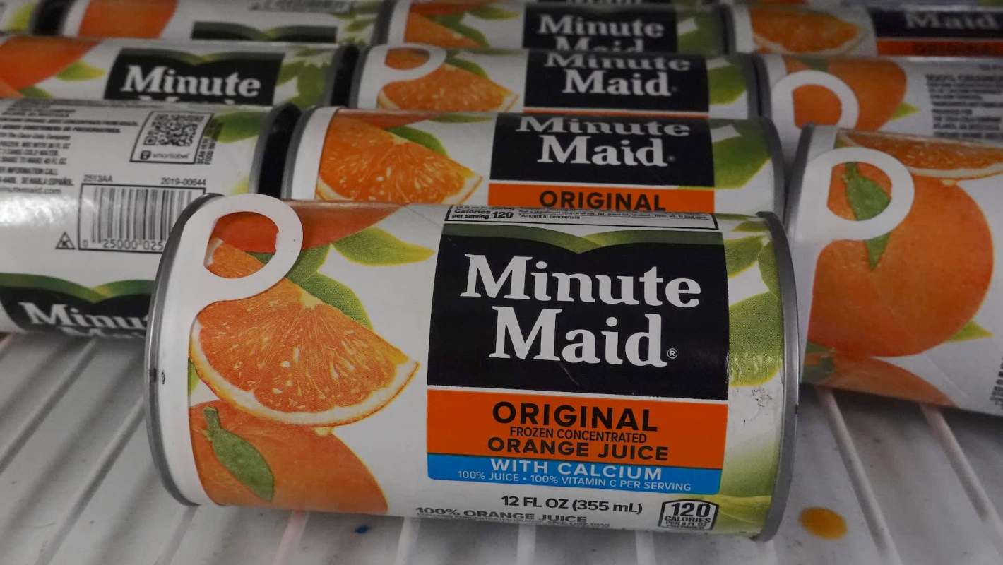 Cans of Minute Maid frozen concentrated orange juice stacked in a cooler, featuring vibrant fruit graphics.