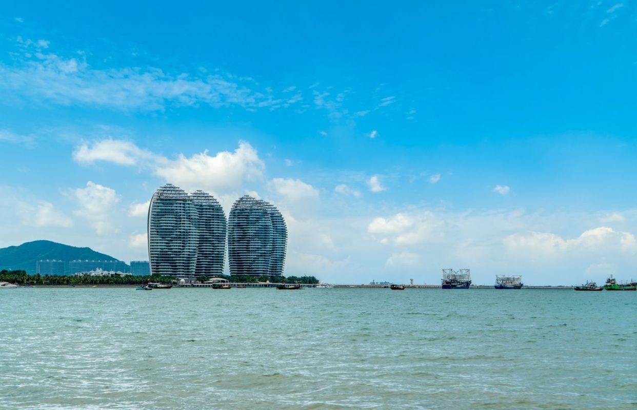 A view of modern, curved skyscrapers by the water under a partly cloudy blue sky.