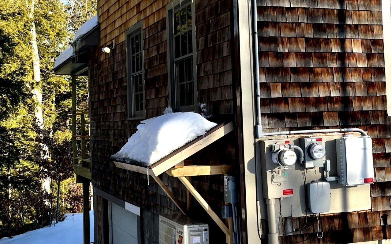 A wooden house exterior with snow on the roof and electrical meters on the wall.