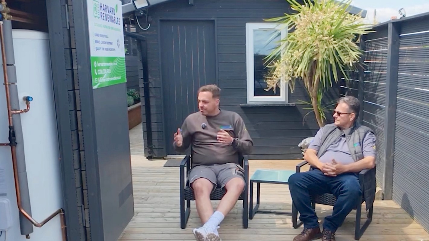 Two men sitting on chairs on a deck, discussing heat pumps and HVAC in the UK.
