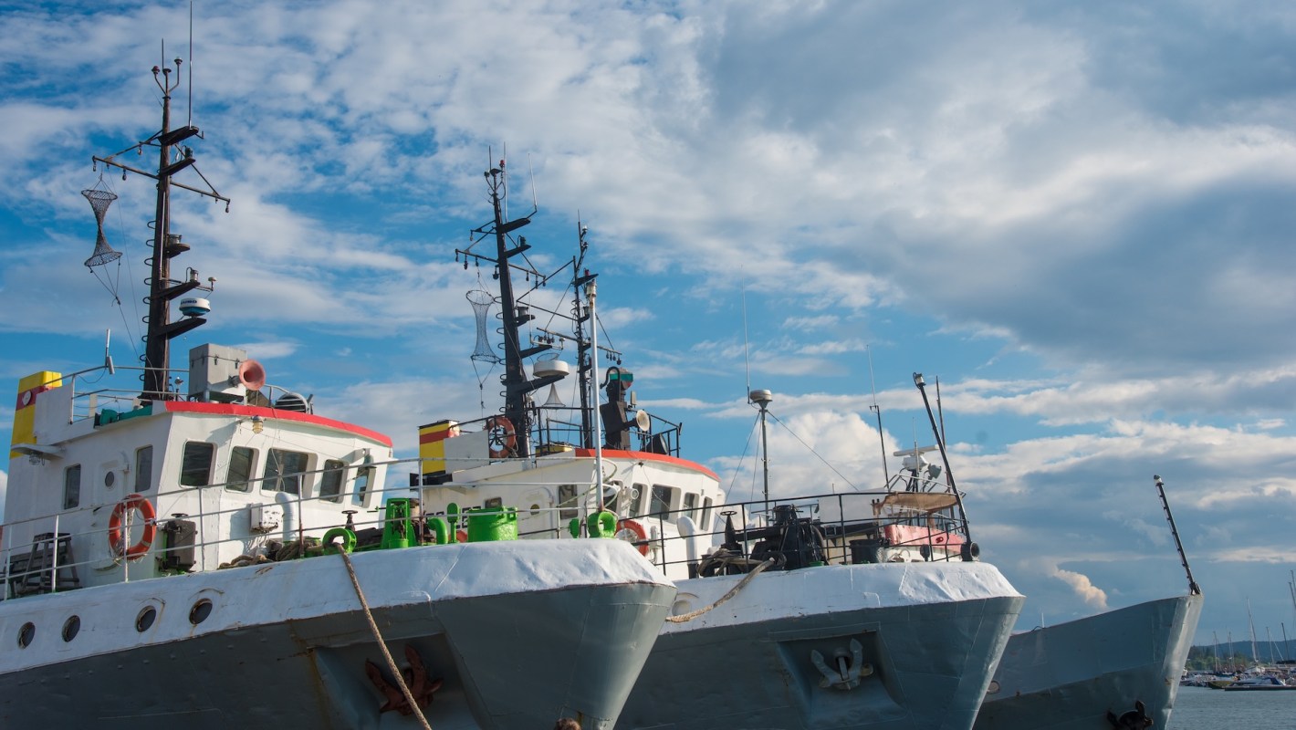 Two fishing boats docked at a harbor under a partly cloudy blue sky.