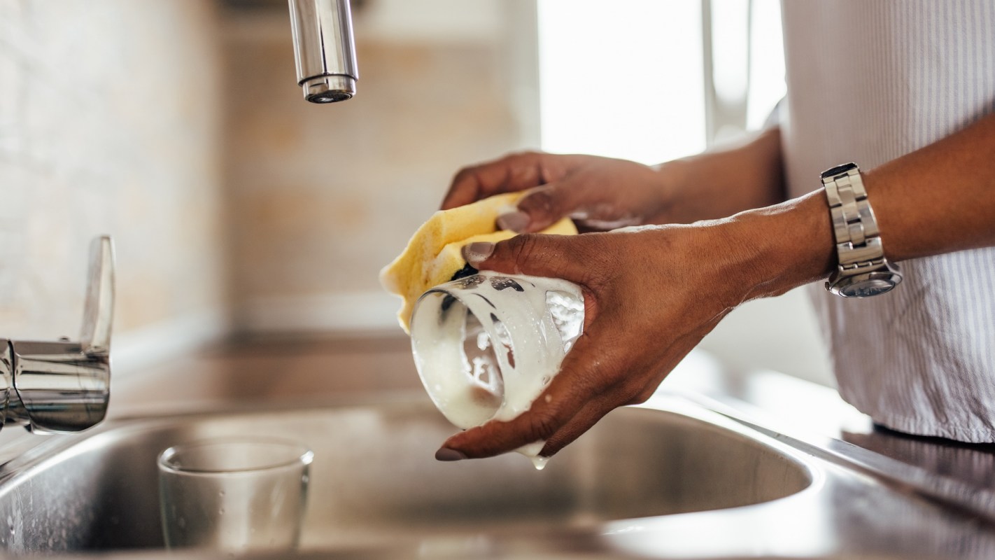 Person washing glass with kitchen sponge.