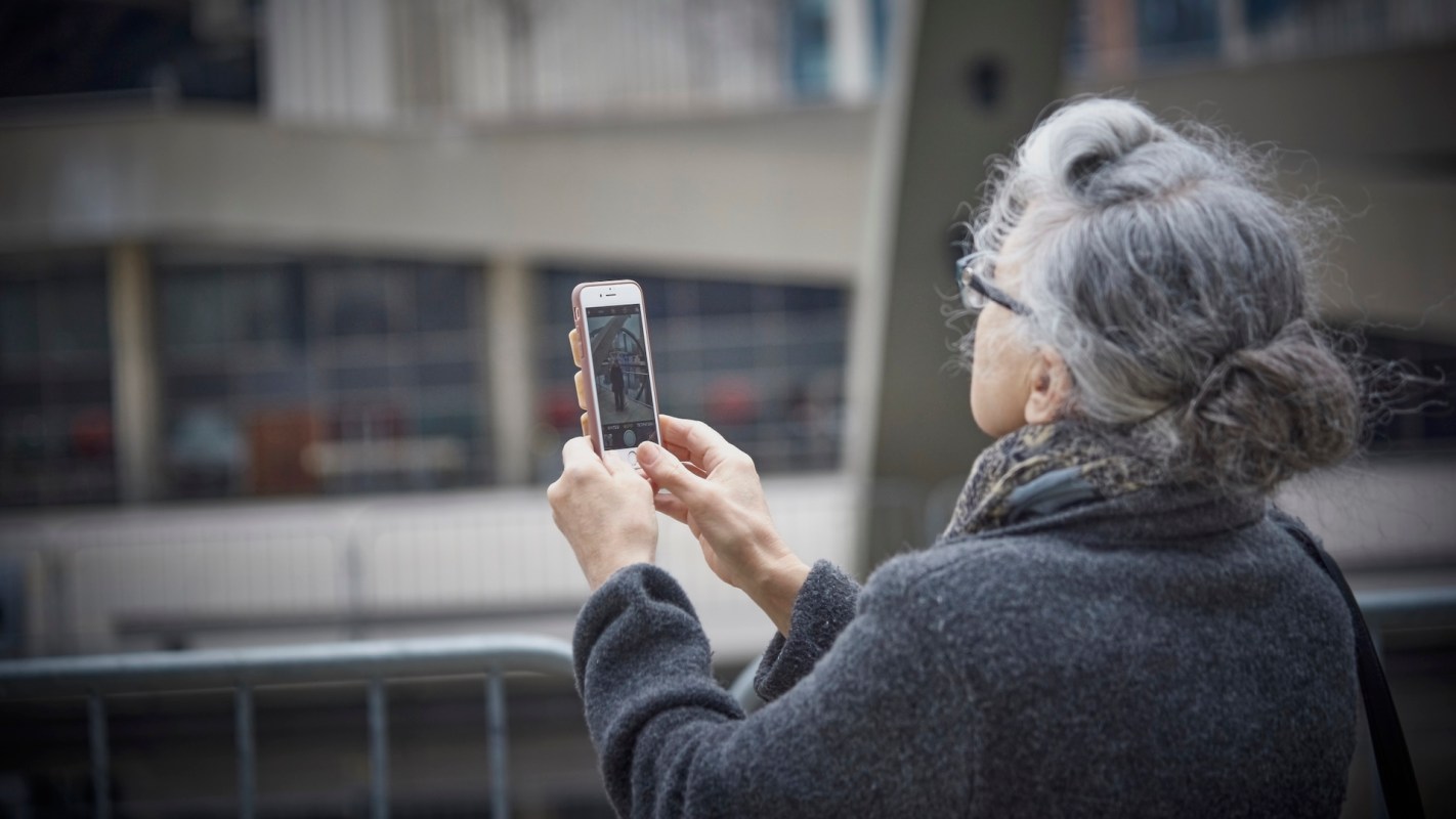 An older woman is holding up a mobile phone.