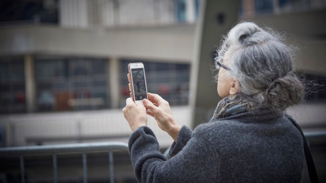 An older woman is holding up a mobile phone.