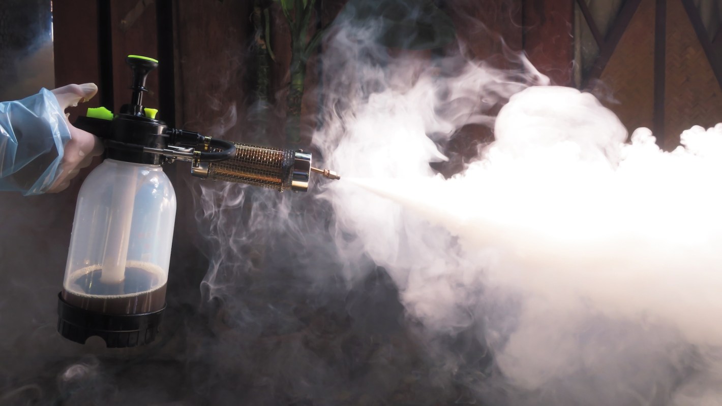 A gloved hand using a machine to spray pesticide.