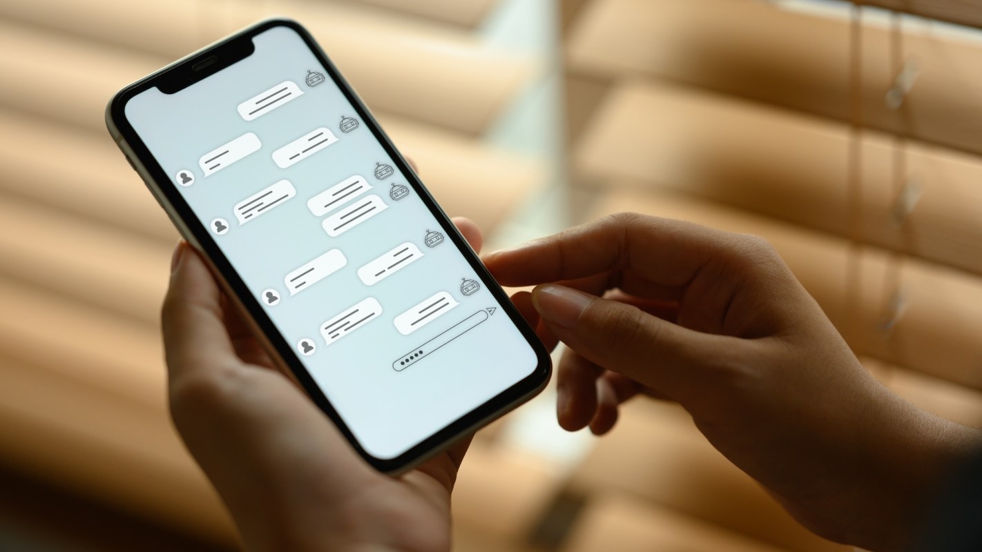A person holding a smartphone displaying a messaging app with multiple chat bubbles and a text input field.