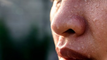 A close-up of a wet face with droplets of water on the nose and lips, reflecting light.