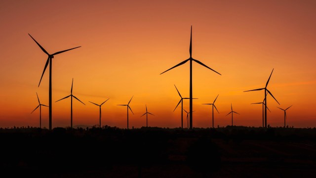 Silhouettes of wind turbines against a vibrant orange and purple sunset sky.