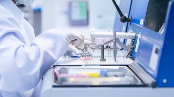 A lab technician in gloves uses tweezers to handle samples on a clean workstation.