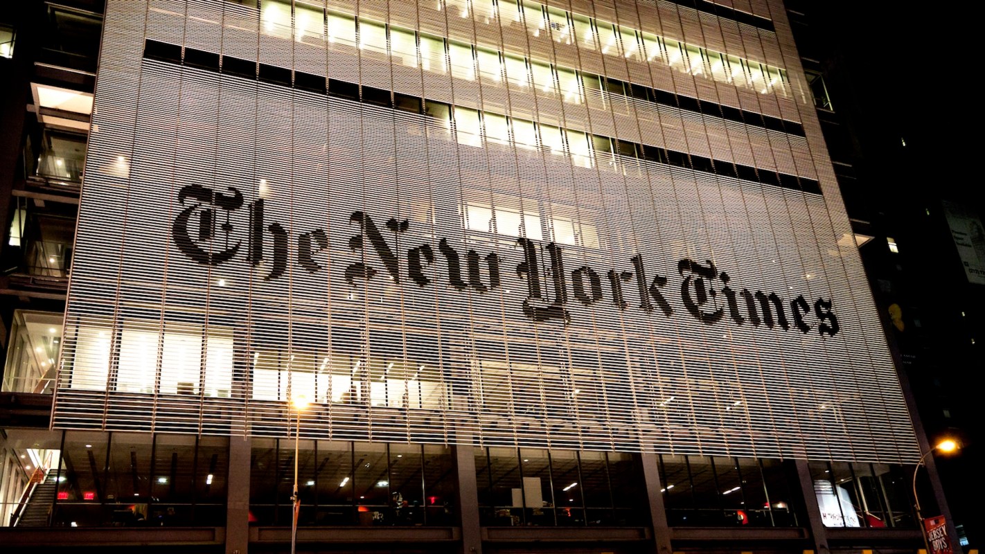 The illuminated facade of The New York Times building at night, showcasing its iconic logo.