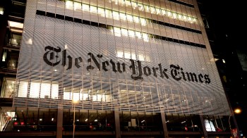 The illuminated facade of The New York Times building at night, showcasing its iconic logo.