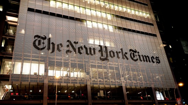 The illuminated facade of The New York Times building at night, showcasing its iconic logo.