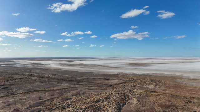 A vast, arid landscape with a salt flat under a bright blue sky dotted with clouds.