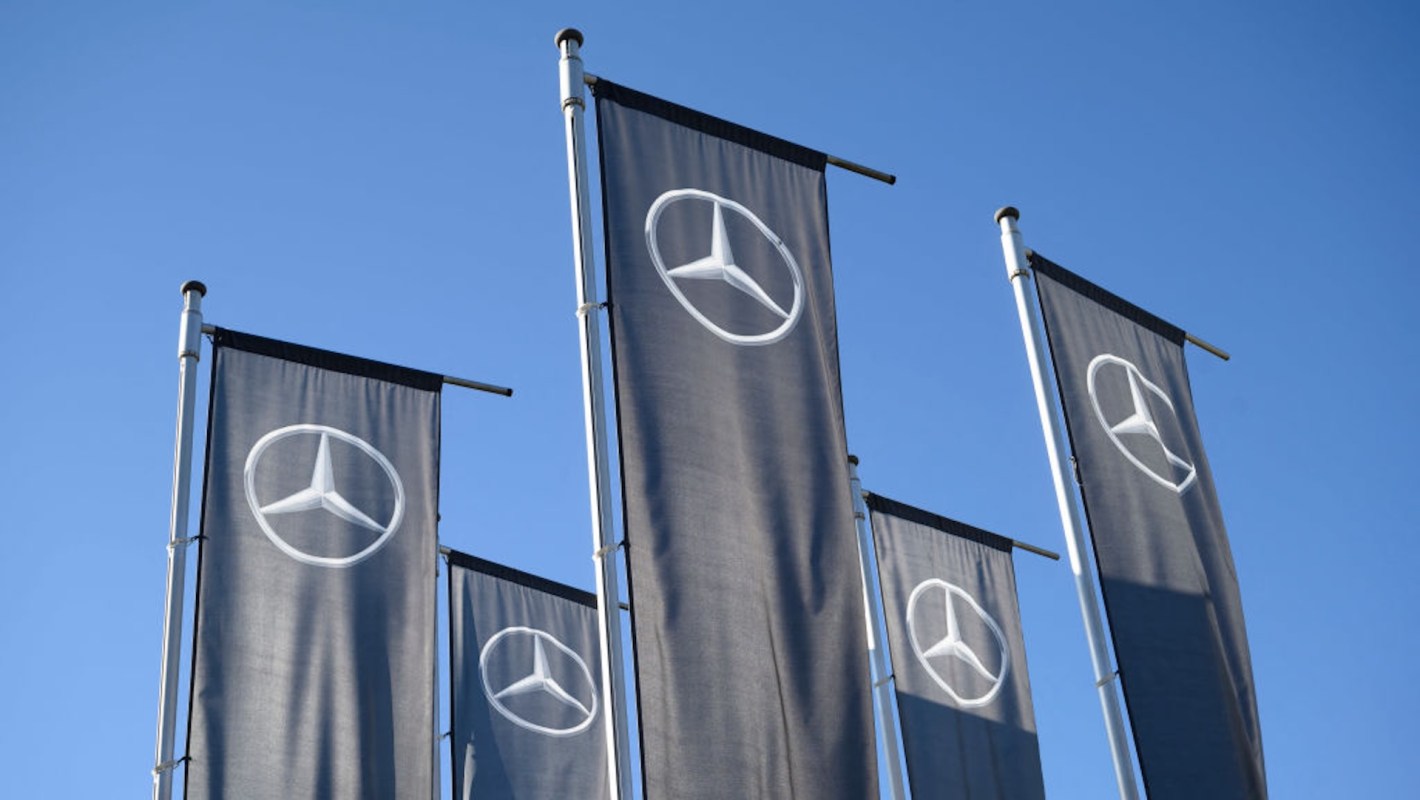 Five flags with the Mercedes-Benz logo against a clear blue sky.
