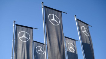 Five flags with the Mercedes-Benz logo against a clear blue sky.