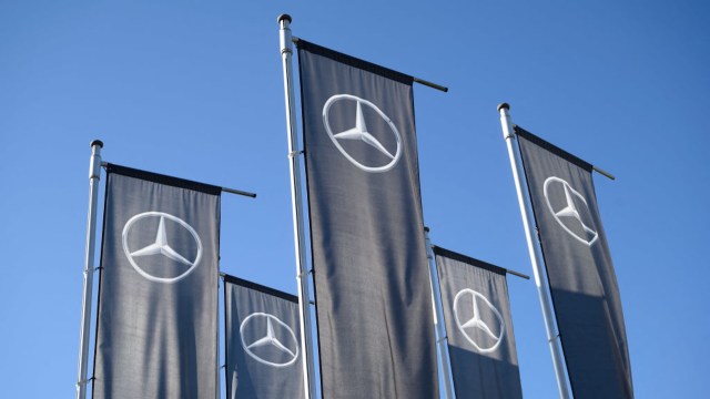 Five flags with the Mercedes-Benz logo against a clear blue sky.