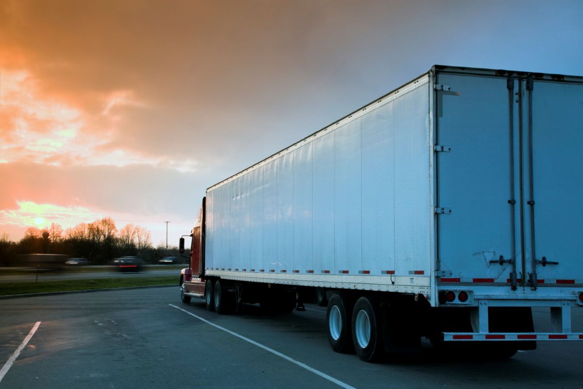 A parked truck with a white trailer is set against a sunset sky with soft orange and blue hues.