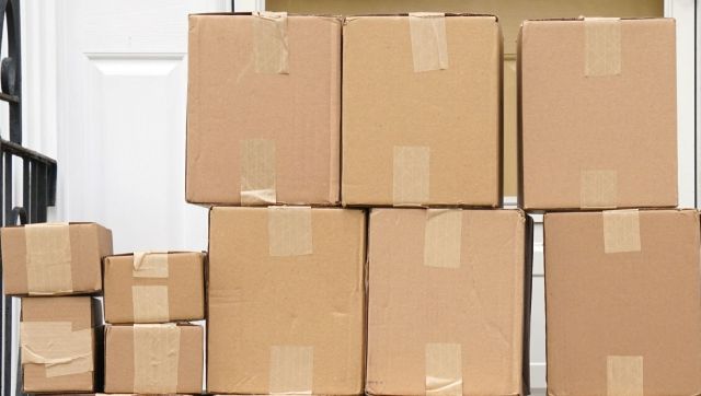 A stack of cardboard boxes of varying sizes placed on a doorstep with a white door in the background.