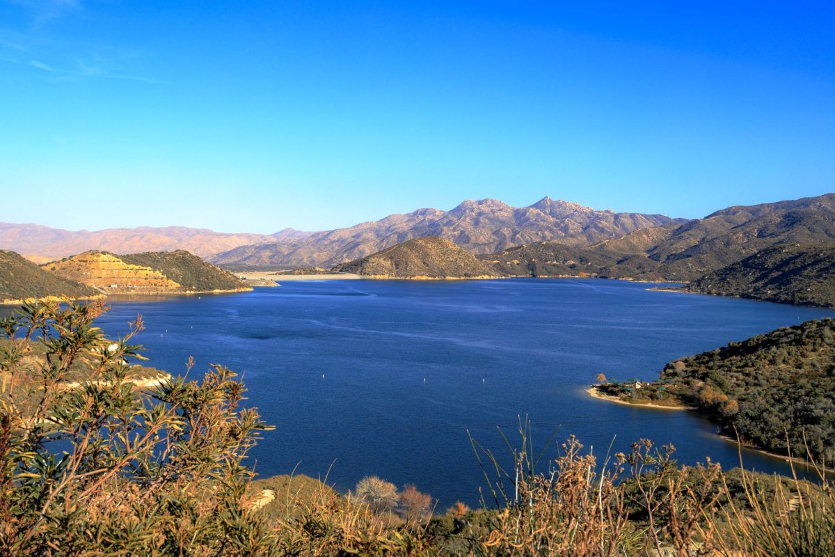 A serene view of a lake surrounded by mountains under a clear blue sky.