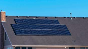 A roof with several solar panels installed, against a clear blue sky.