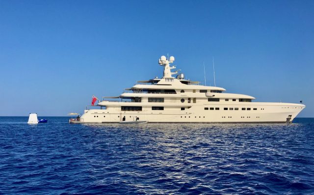 A large luxury yacht anchored in calm blue waters under a clear sky.