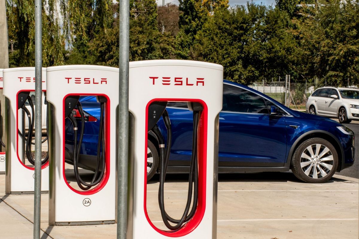 A row of Tesla charging stations with a blue Tesla vehicle parked nearby.