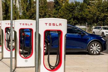 A row of Tesla charger stations with a blue Tesla vehicle parked nearby.