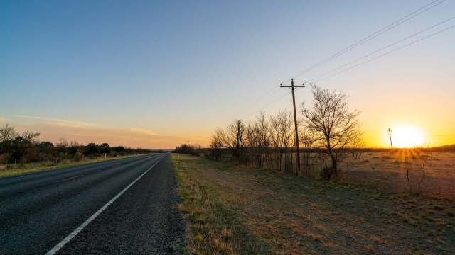 A quiet rural road lined with bare trees and power lines against a sunset sky.