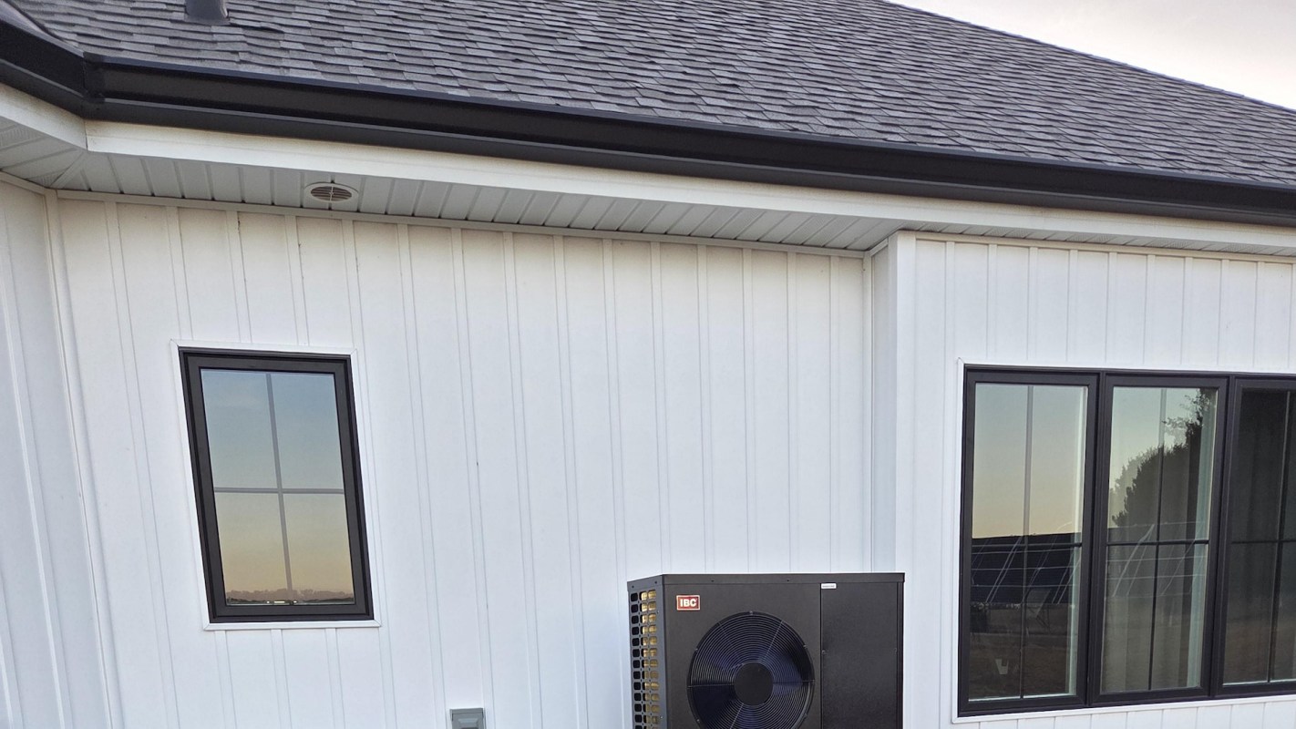 A modern house exterior featuring white paneling, black windows, and an air conditioning unit.