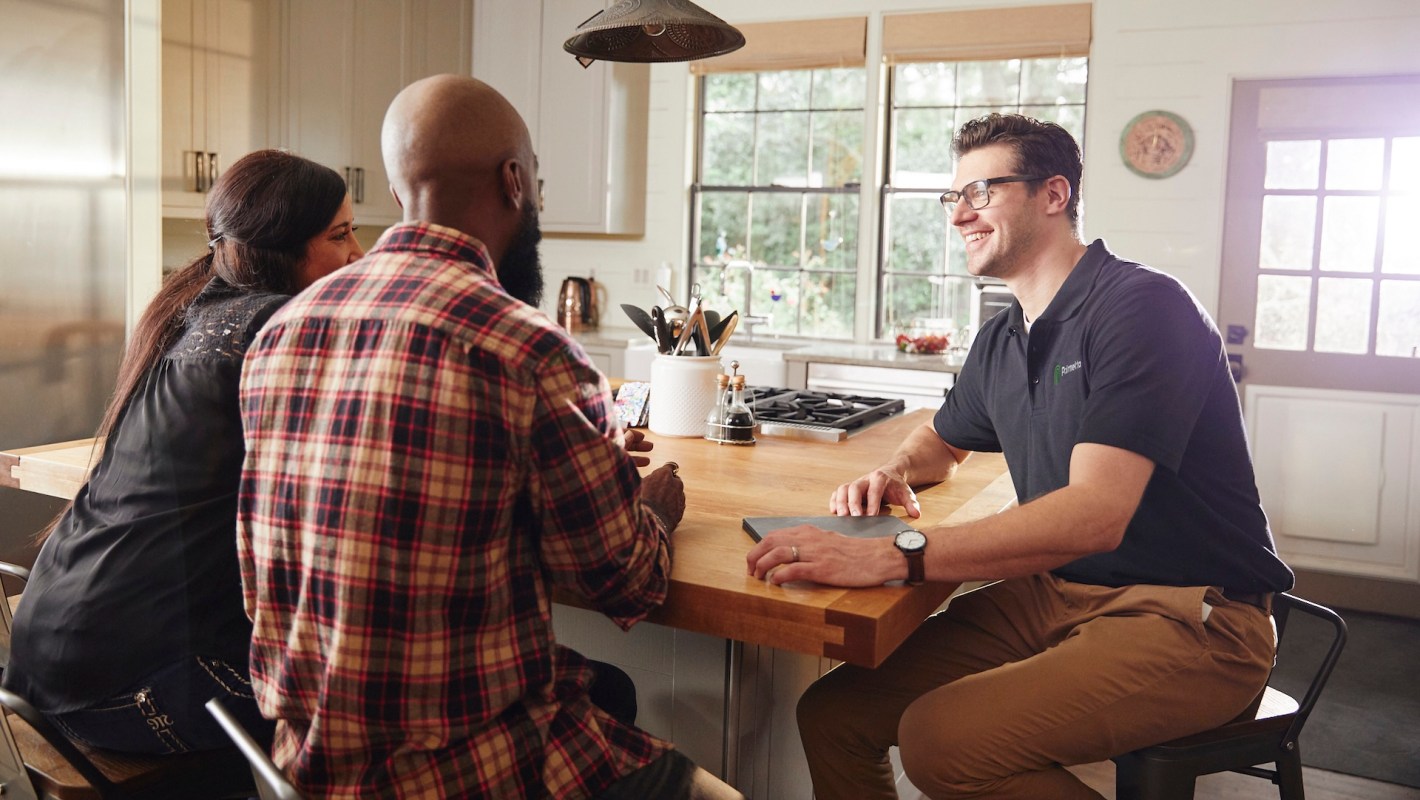 Three people seated at a kitchen table engaged in a friendly conversation.