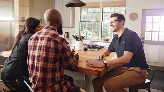 A Palmetto Solar employee talking to two people in a kitchen.