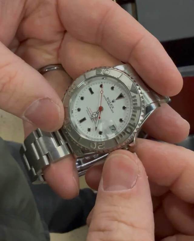 A person is holding a watch with a Rolex logo.