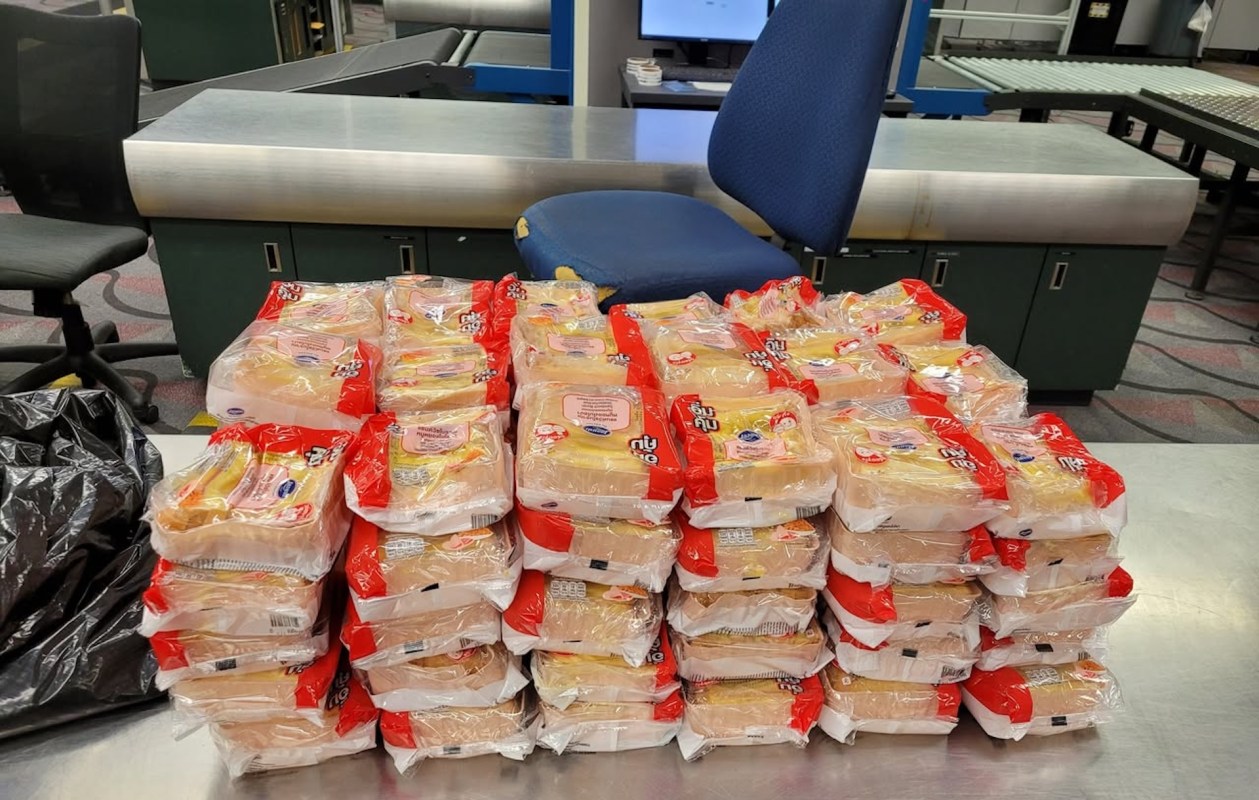 A stack of neatly arranged packages sits on a table near a chair in an backroom setting at an airport.