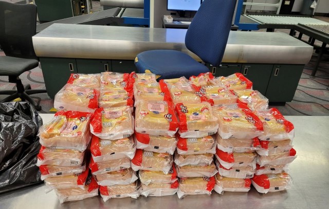 A stack of packaged sandwiches sits on a table at customs at an airport.