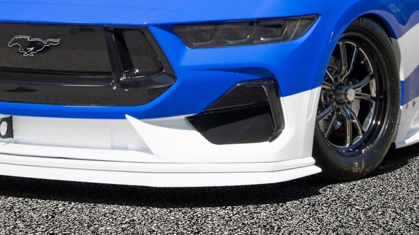 A bottom portion of blue-and-white Ford Mustang, with the chrome horse emblem on the car's grille.