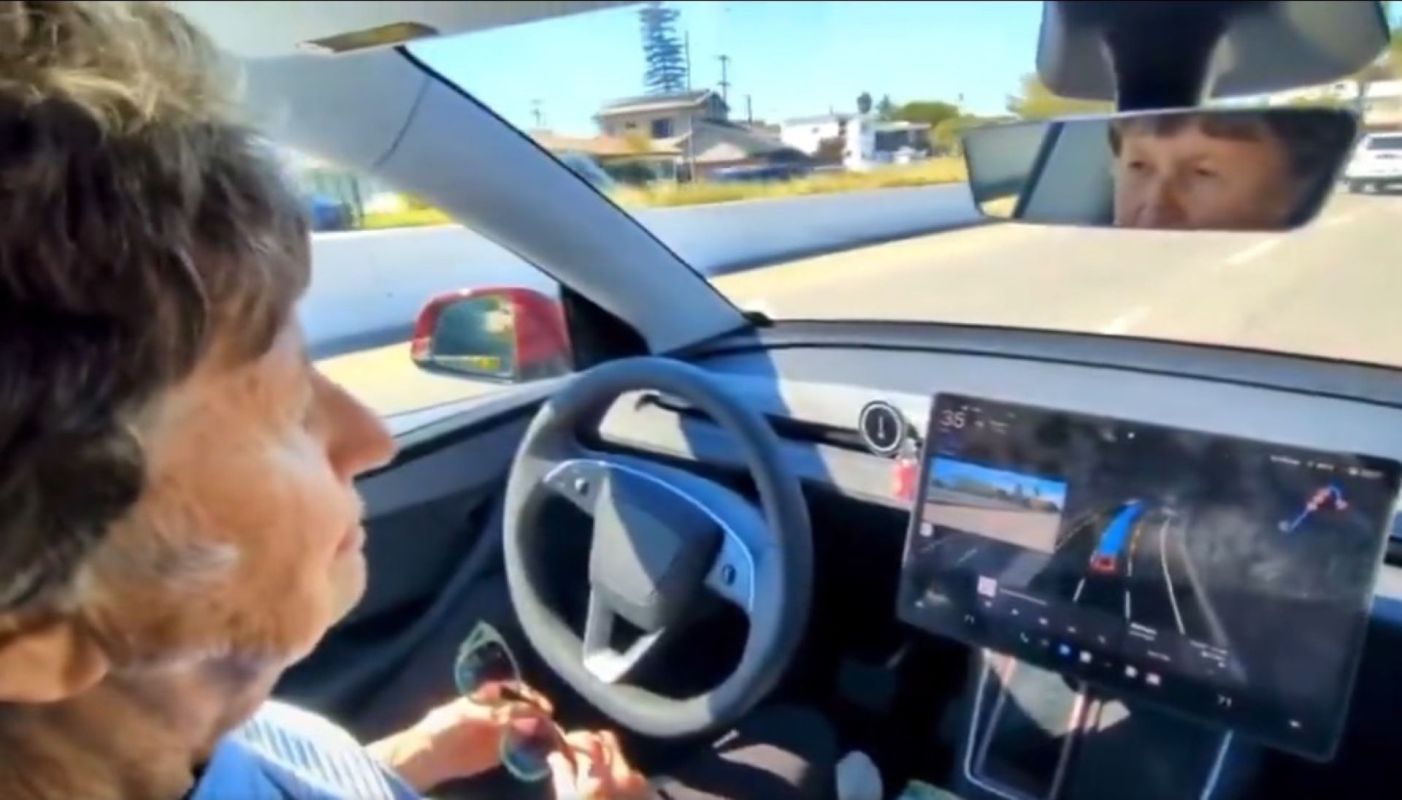 An old woman sits in a self-driving Tesla.